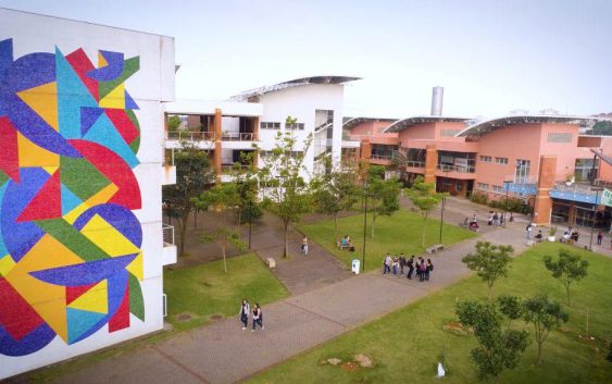 campus de faculade com prédios brancos e alunos no gramado